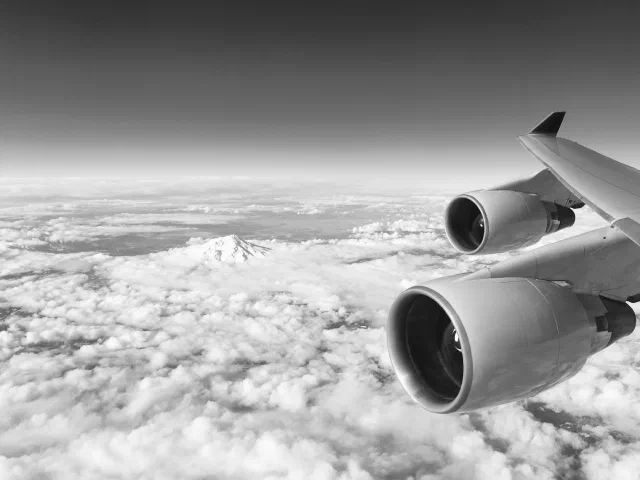 The engines and wing of a Boeing 747 above the clouds, with Mount Shasta in the distance