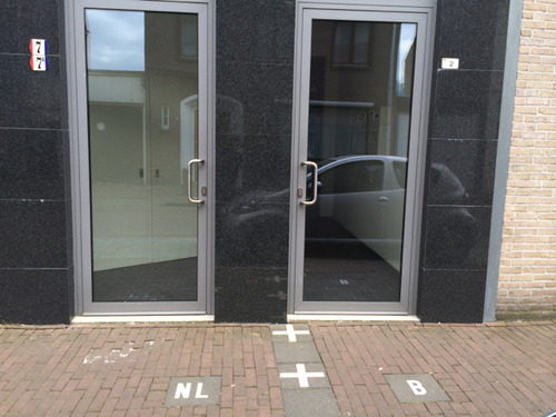 Two glass front doors a metre apart on the same building, with NL marked on the pavement in front of one and B in front of the other