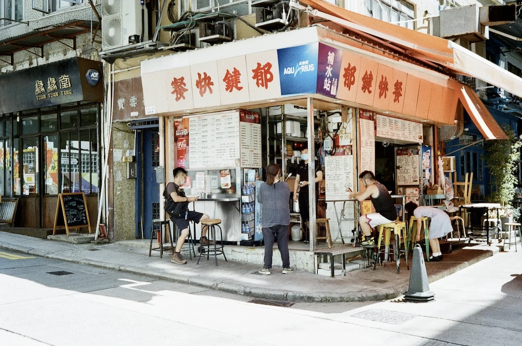 A corner cha chaan teng cafe with an orange awning and customers at the counter