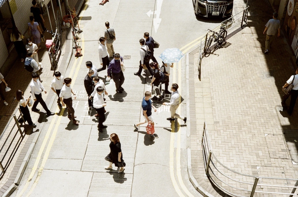 Pedestrians crossing a sunlit intersection, photographed from above