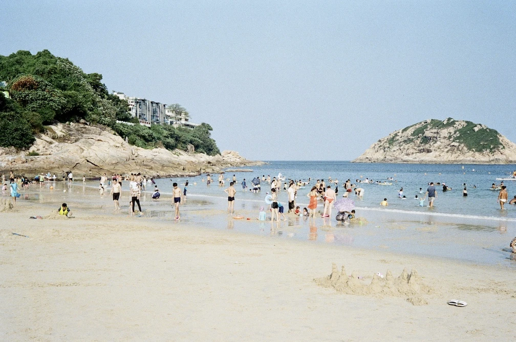 Shek O beach on a sunny day with swimmers in the water and a rocky headland behind