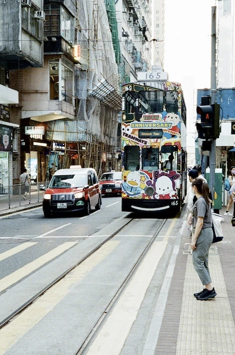 A double-decker tram approaching head-on down a street between tall buildings