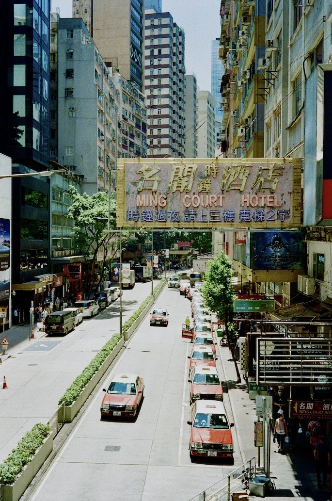 A Wan Chai street with red taxis, dense signage and a hotel sign overhead