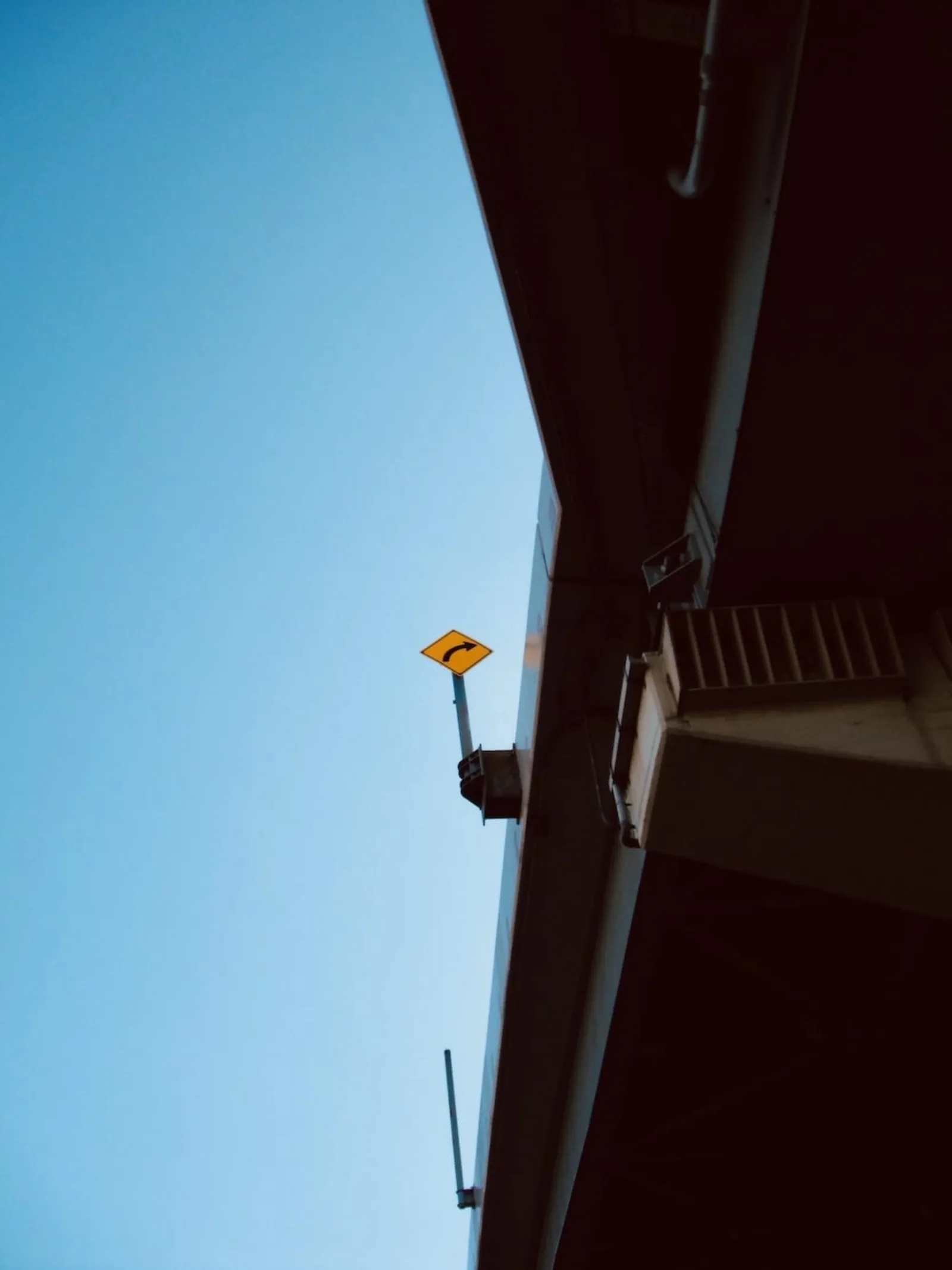 A deep blue sky with the edge of a building and a small sign in the corner of the frame