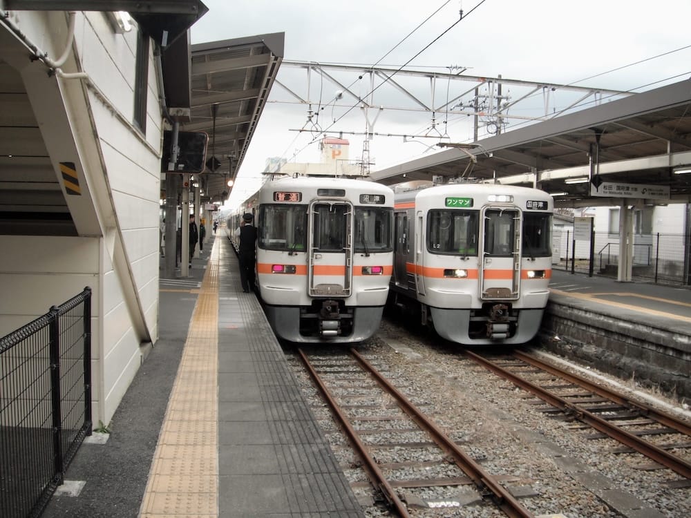 Two JR commuter trains with orange stripes waiting at a station platform