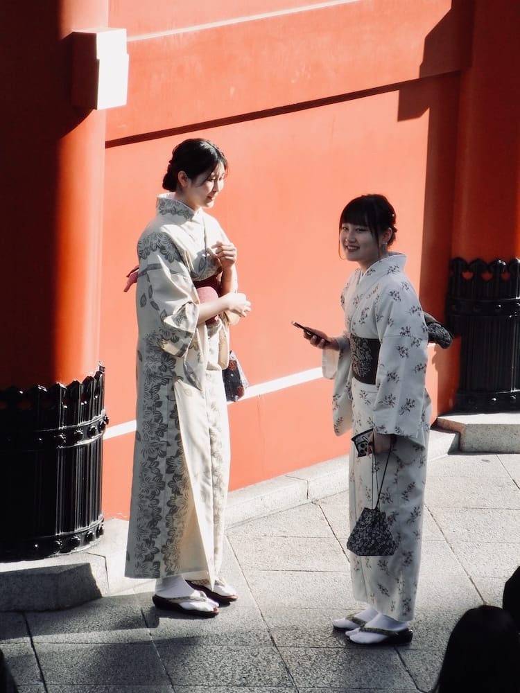 Two women in kimono talking beside the red pillars of Senso-ji temple