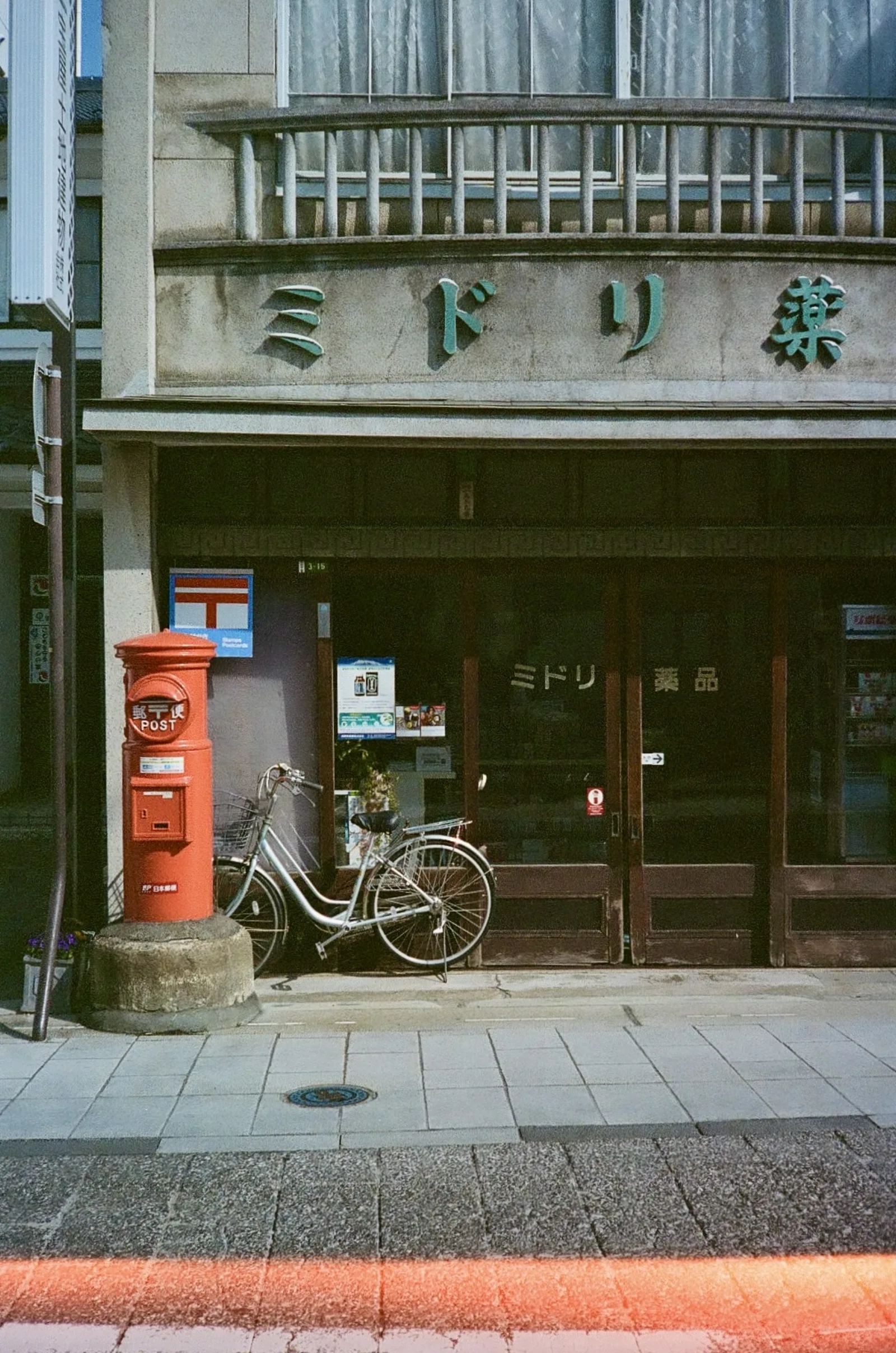 A shopfront with a green Midori sign, a red Japanese post box and a parked bicycle
