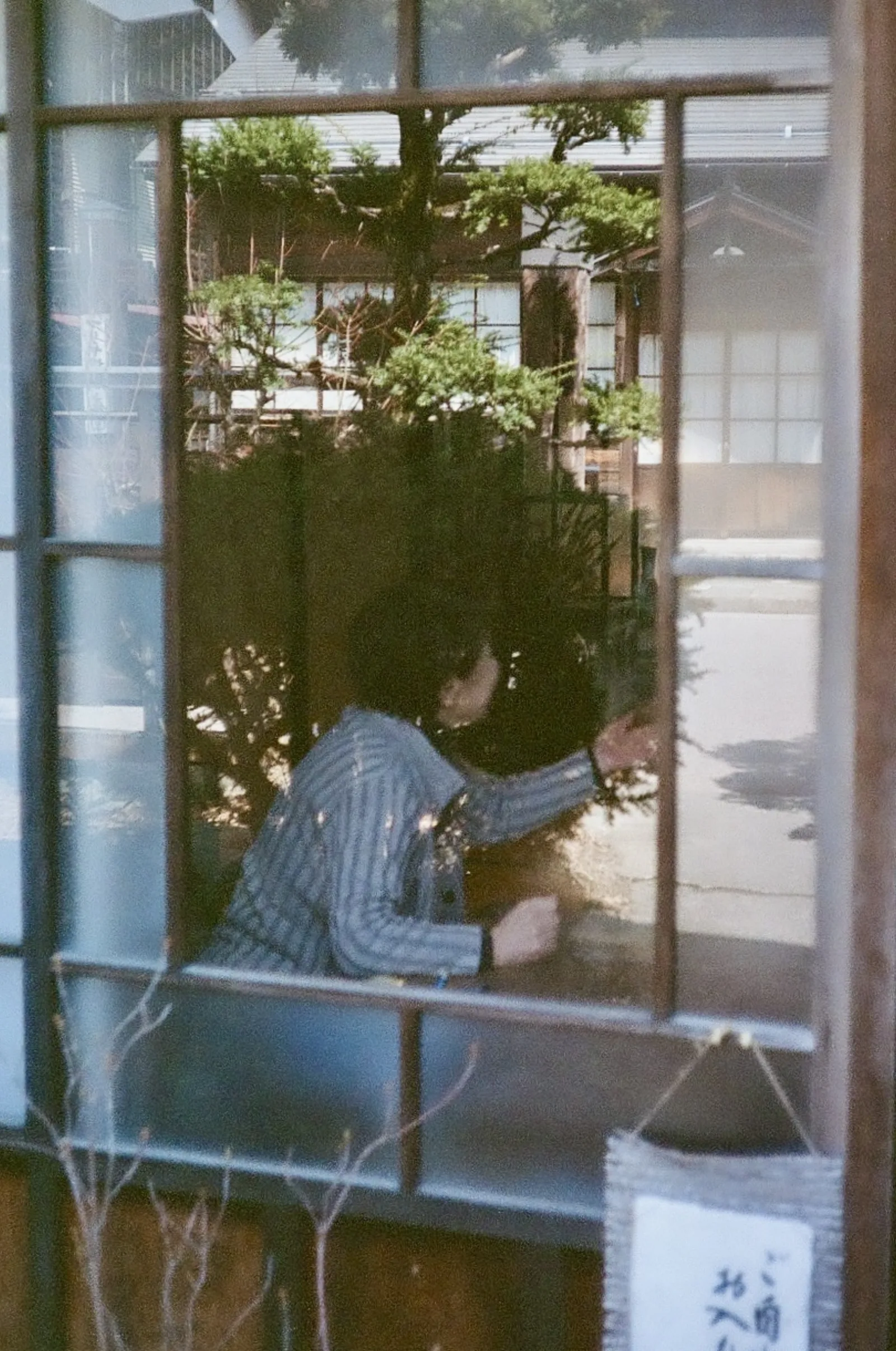 A person seen through a window, with a wooden building reflected in the glass