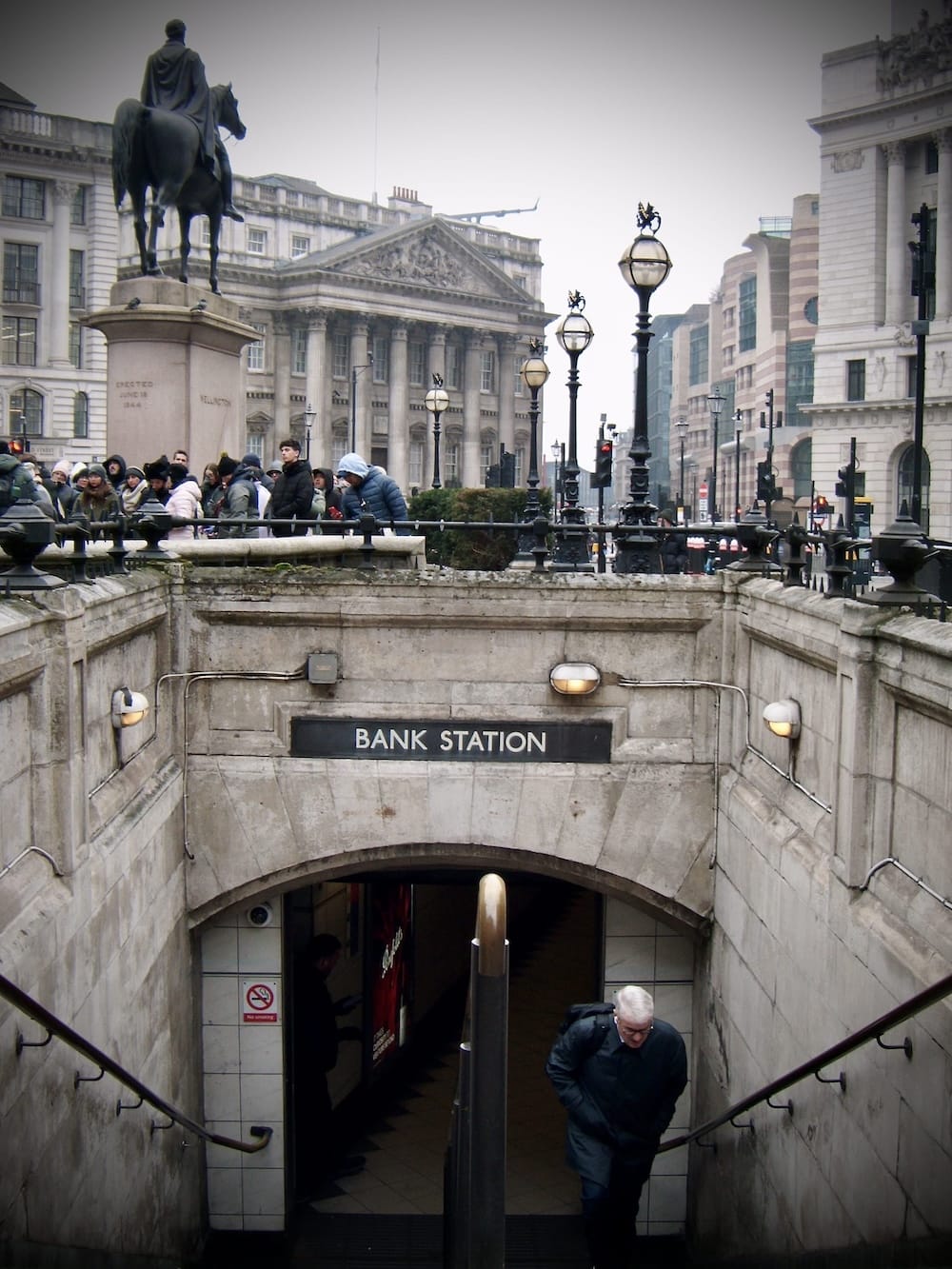 The stone entrance to Bank underground station with a man climbing the steps