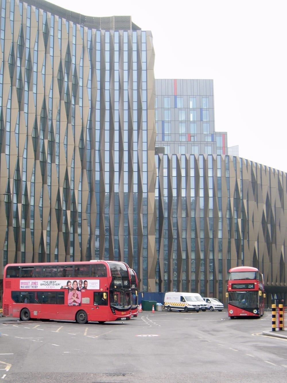 Two red double-decker buses in front of a modern faceted glass office building