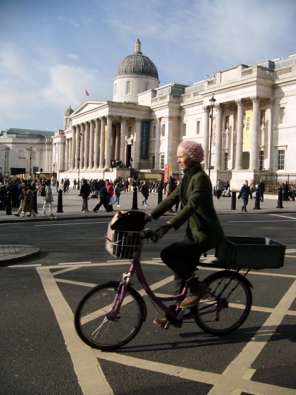 A cyclist crossing the road in front of the National Gallery at Trafalgar Square