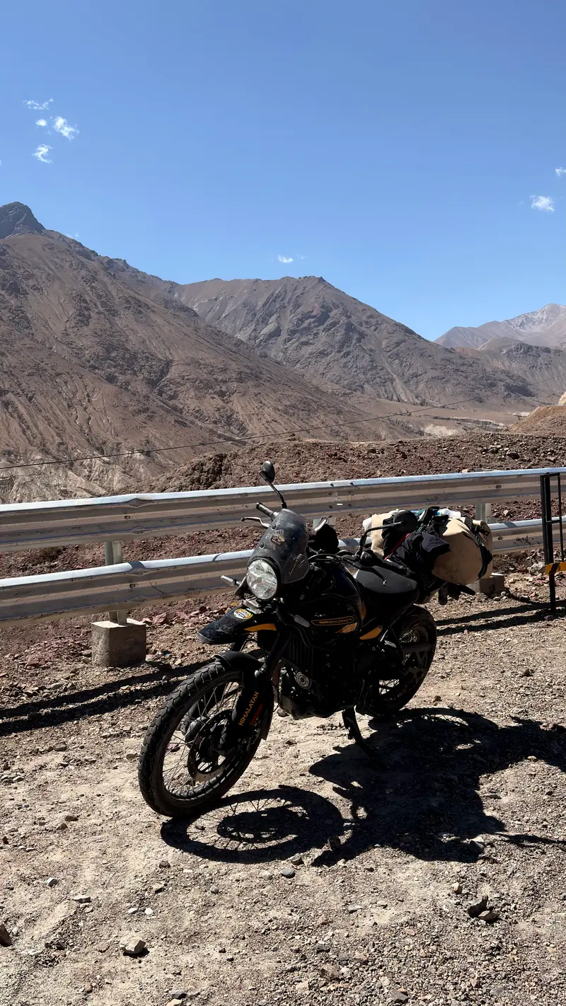 A loaded Royal Enfield Himalayan parked at a guardrail overlooking the valley