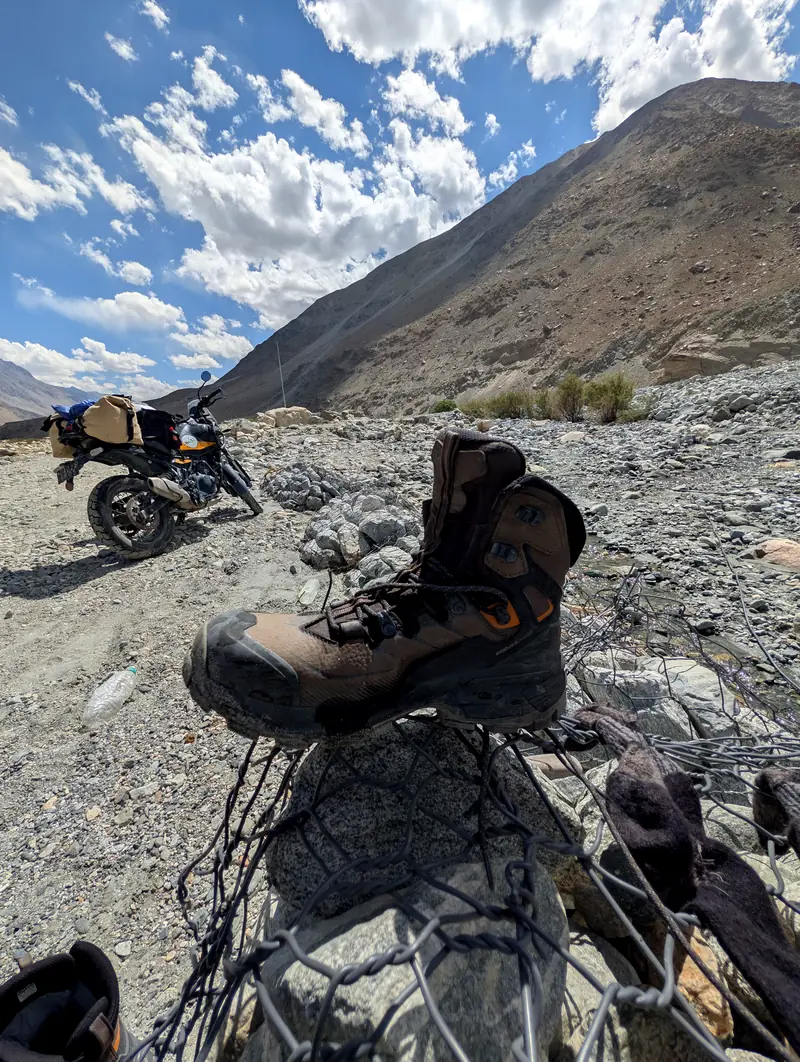 A wet hiking boot drying on a wire gabion beside the parked motorcycle