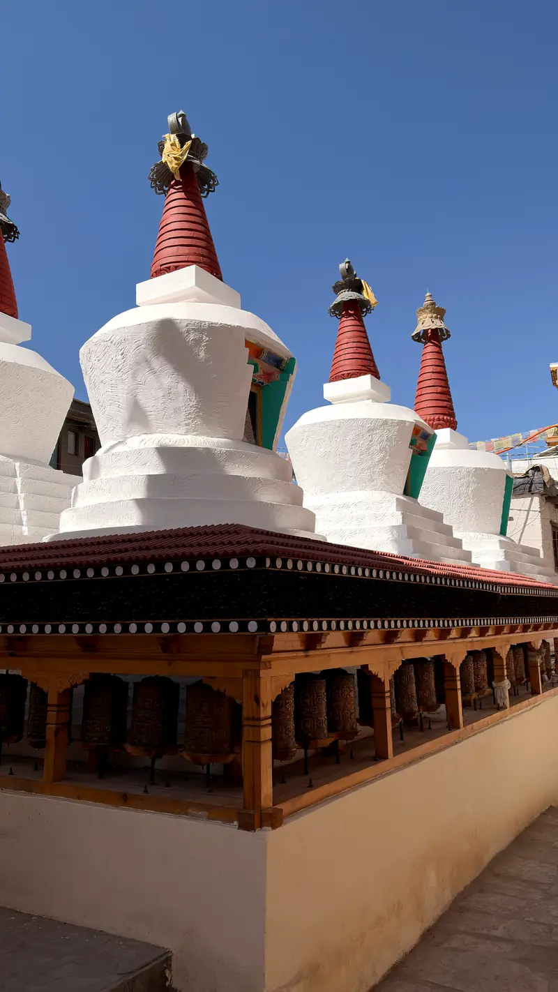 A row of white chortens with red spires above a line of prayer wheels