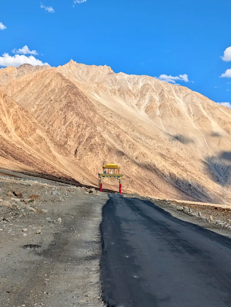 The painted welcome gate of Diskit dwarfed by an immense scree slope behind it