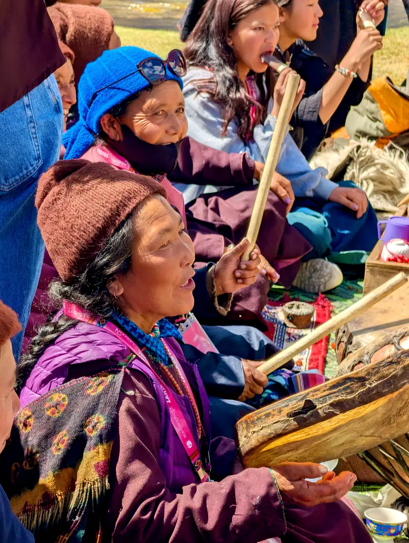 Seated women singing and beating hand drums at the festival