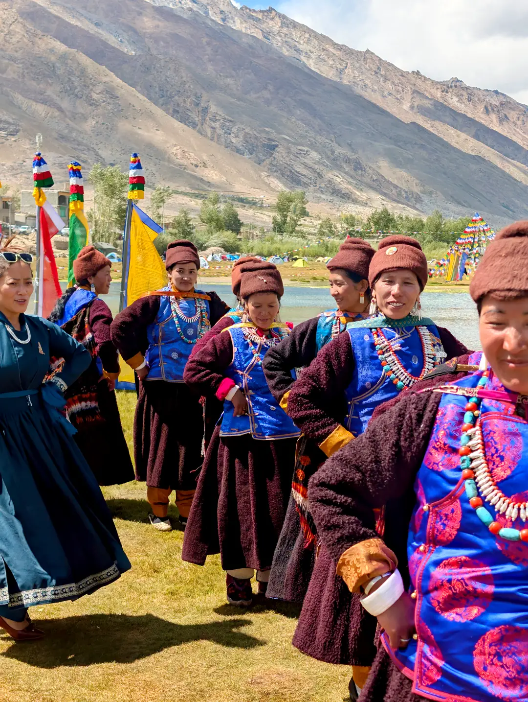 Women in traditional Zanskari dress, woolen robes and turquoise jewellery, gathered by the water with ceremonial flags