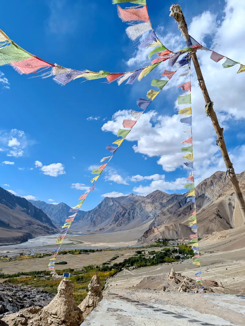 Prayer flags strung from a pole above a green village with chortens far below