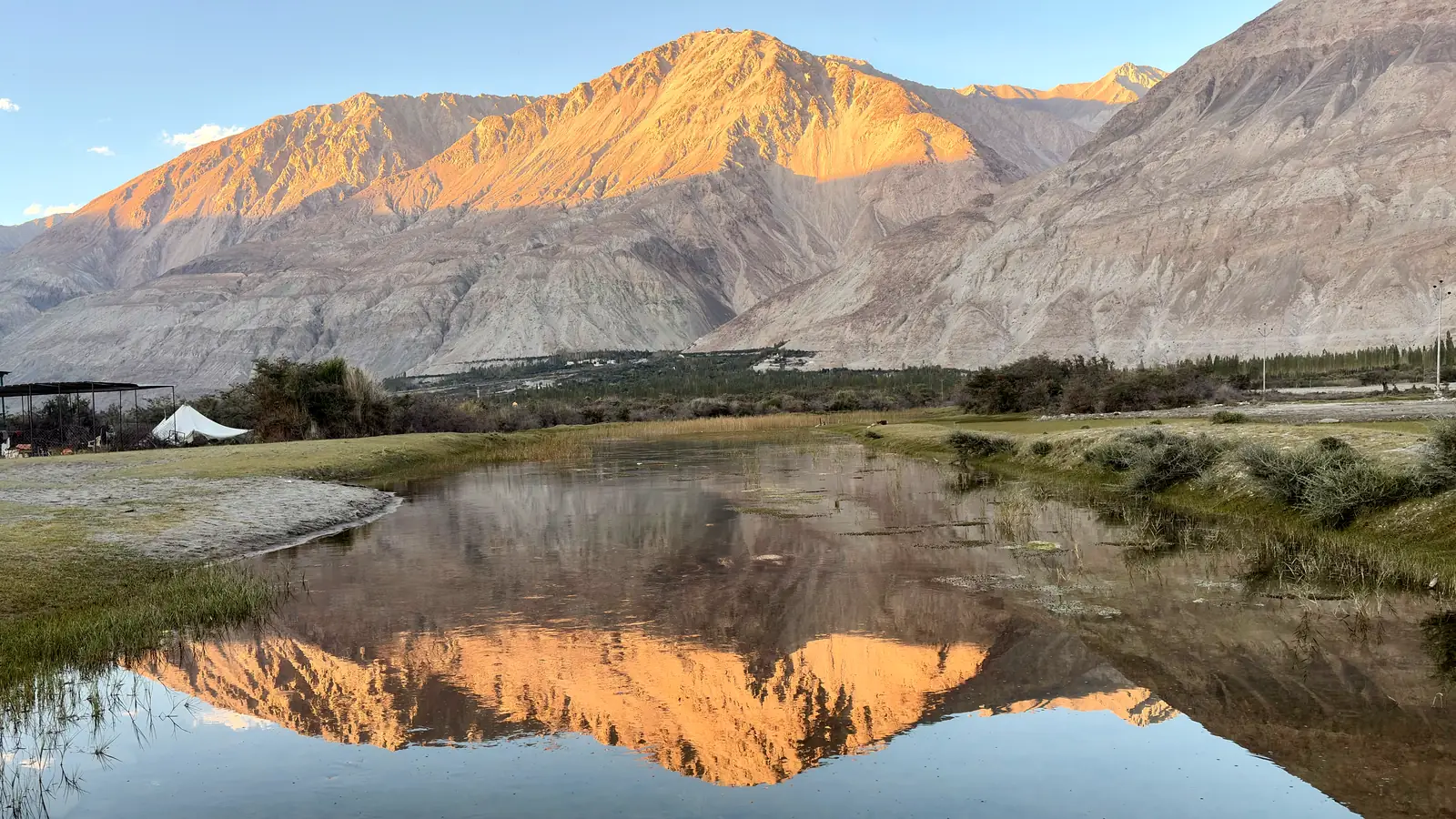 Evening light on a bare mountain range reflected in still water in the Nubra Valley