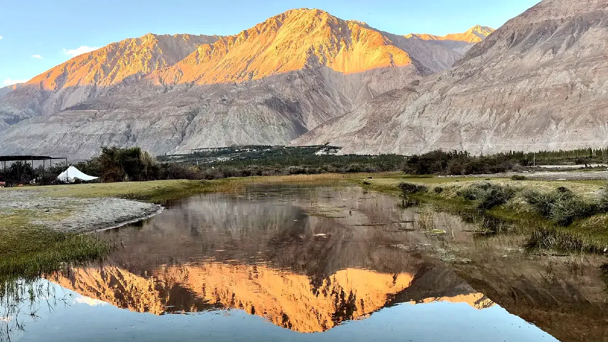 Evening light on a bare mountain range reflected in still water in the Nubra Valley