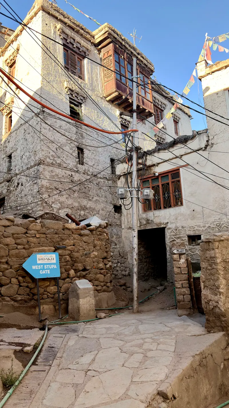 A whitewashed lane in Leh old town with a carved wooden balcony overhead