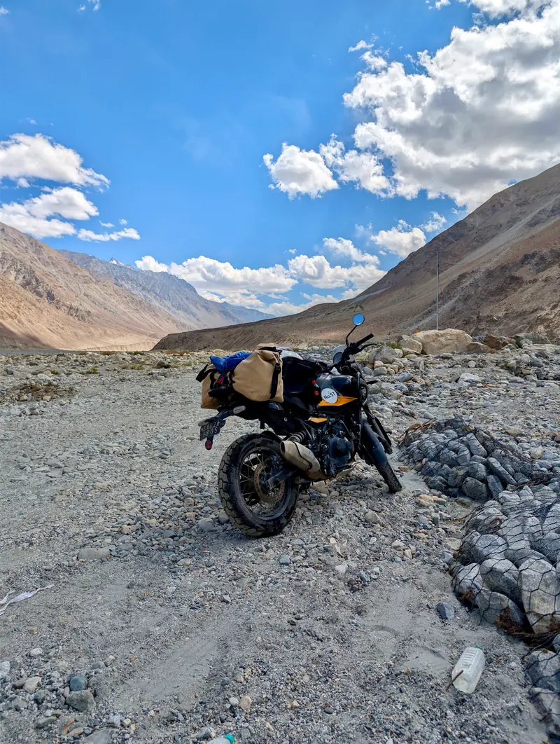 The packed motorcycle in morning light on the Shyok road, mountains behind