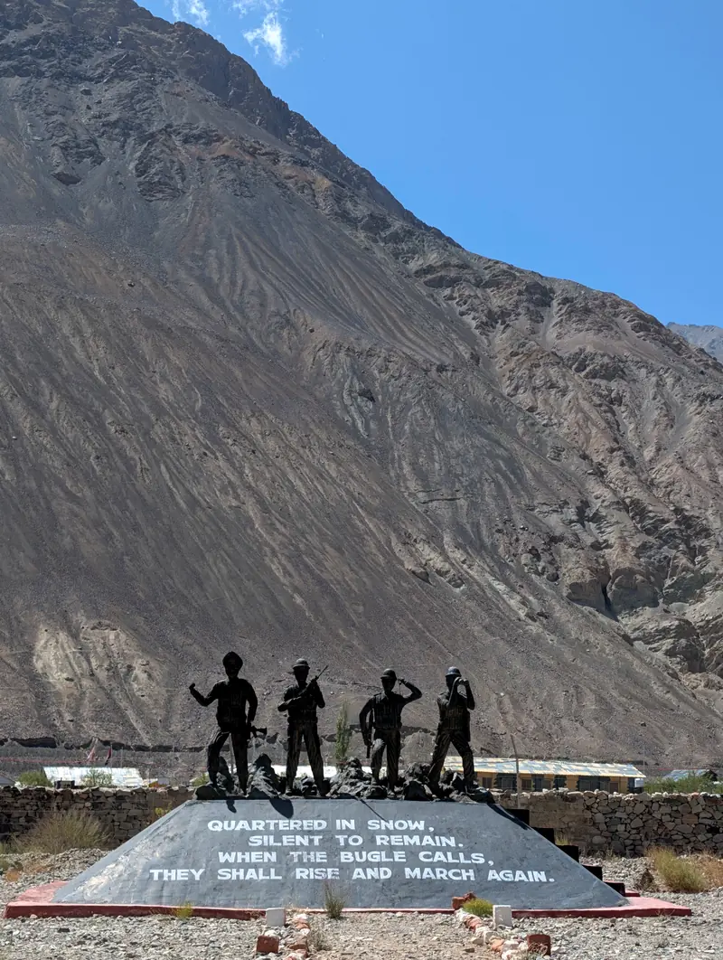 Bronze statues of four soldiers on a stone memorial beneath a huge mountainside