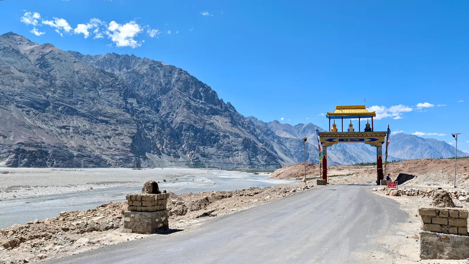 Panorama of the wide braided Shyok river valley with a welcome gate on the road