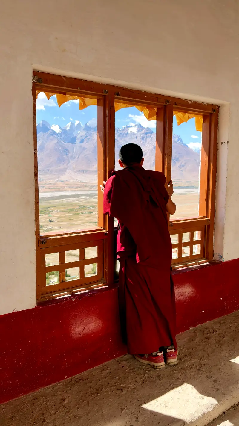 A monk leans on a window sill looking out over the valley and distant peaks