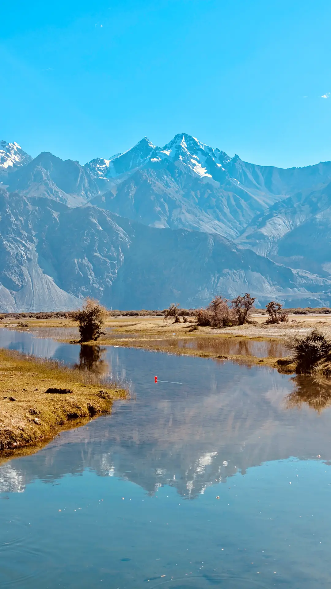 Snow peaks and golden evening mountains reflected in a still pond near Sumur