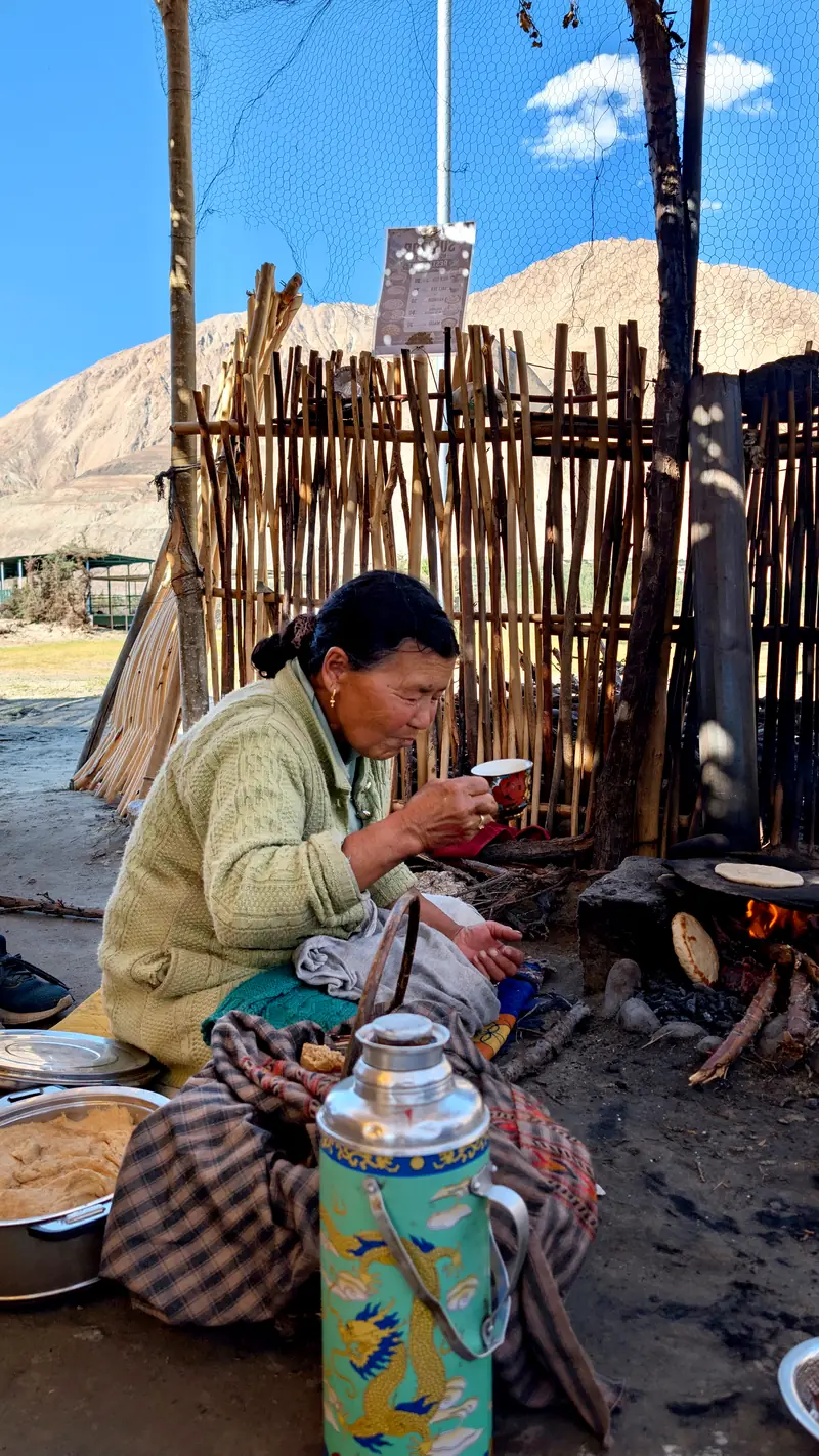 A woman making flatbread over an open wood fire beside a large patterned thermos