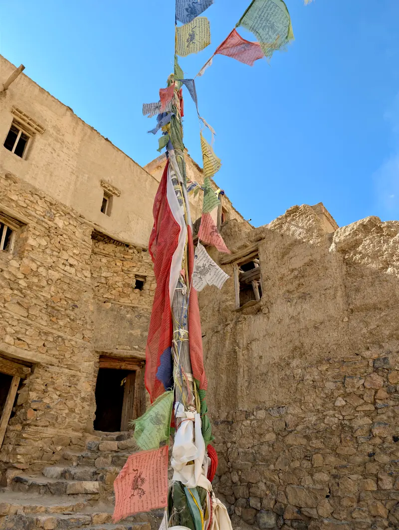 A stone-walled village lane with prayer flags and old houses